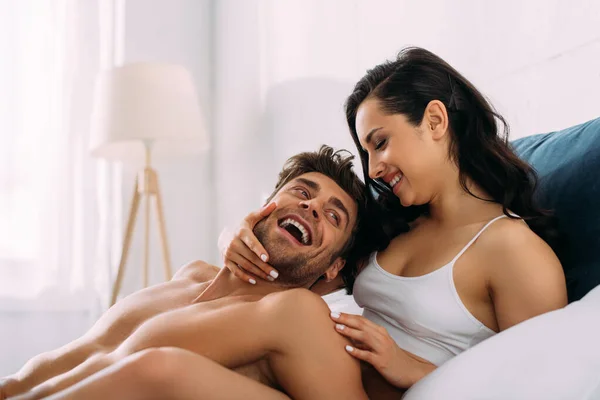 Mulher sorrindo e abraçando homem animado na cama no quarto — Fotografia de Stock