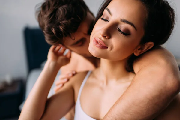 Foco seletivo do homem abraçando e beijando menina atraente com olhos fechados no quarto — Fotografia de Stock
