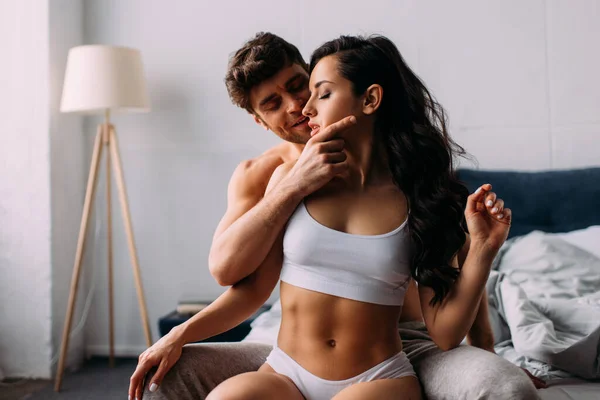 Man smiling, touching female face and sitting near girl with closed eyes on bed in bedroom — Stock Photo