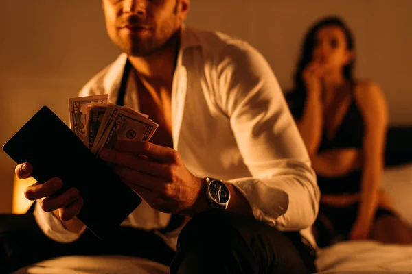 Селективный фокус бизнесмена с кошельком и деньгами возле проститутки на кровати в спальне — стоковое фото