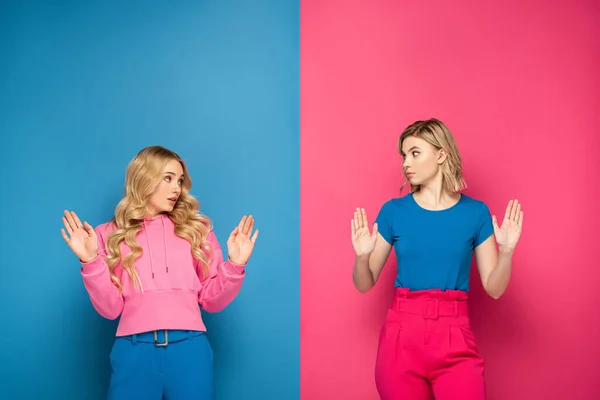 Verwirrte blonde Mädchen zeigen Stop-Geste auf rosa und blauem Hintergrund — Stockfoto