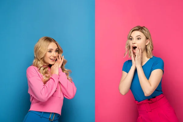 Smiling and shocked blonde girls looking away on pink and blue background — Stock Photo