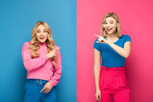 Chicas rubias sonrientes señalándose con los dedos sobre fondo azul y rosa - foto de stock