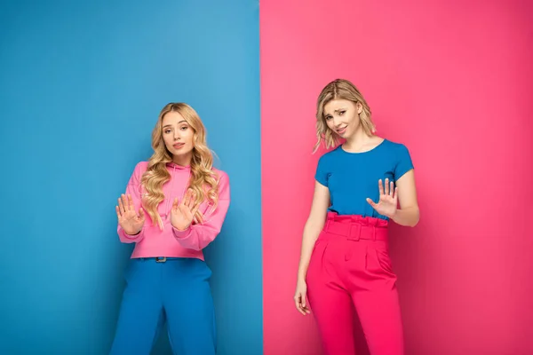 Beautiful blonde women showing stop gesture on pink and blue background — Stock Photo