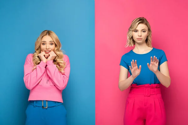 Lächelnde Frau blickt in die Kamera neben blonder Schwester und zeigt Stoppschild auf blauem und rosa Hintergrund — Stockfoto