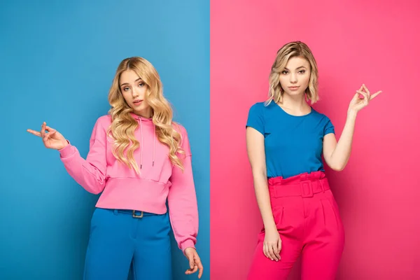 Beautiful blonde sisters pointing with fingers on pink and blue background — Stock Photo