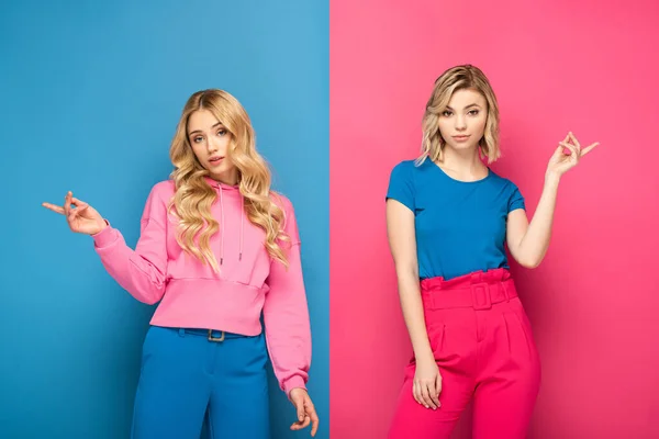 Hermosas hermanas rubias señalando con los dedos sobre fondo rosa y azul - foto de stock