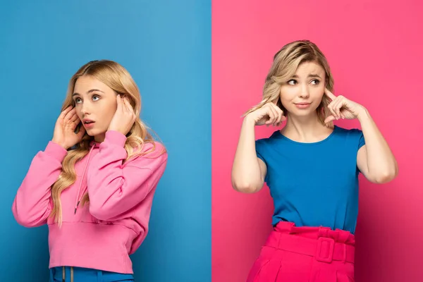 Chicas rubias atractivas cubriendo orejas y mirando hacia otro lado sobre fondo rosa y azul - foto de stock