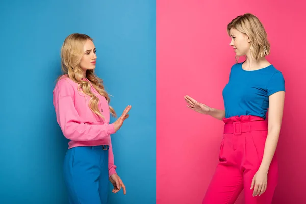 Offended blonde sisters showing stop gesture on pink and blue background — Stock Photo