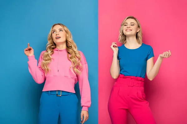 Blondes Mädchen mit Idee in der Nähe positiver Schwester auf rosa und blauem Hintergrund — Stockfoto