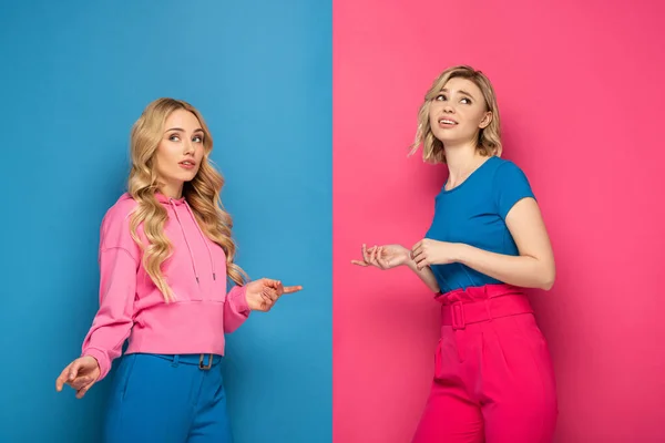 Hermanas rubias señalándose entre sí con los dedos sobre fondo rosa y azul - foto de stock