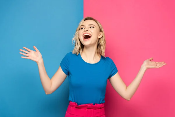 Positive blonde Frau schaut weg auf rosa und blauem Hintergrund — Stockfoto