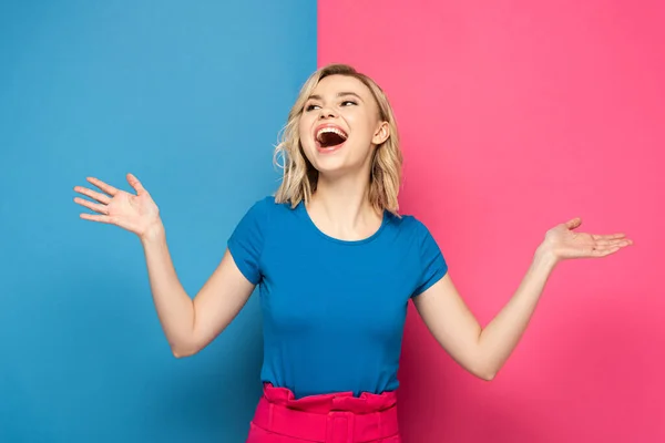 Mujer rubia positiva mirando hacia otro lado sobre fondo rosa y azul - foto de stock