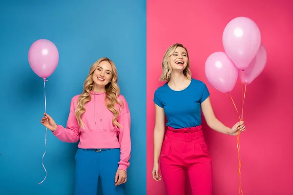 Alegres chicas rubias sosteniendo globos sobre fondo azul y rosa - foto de stock