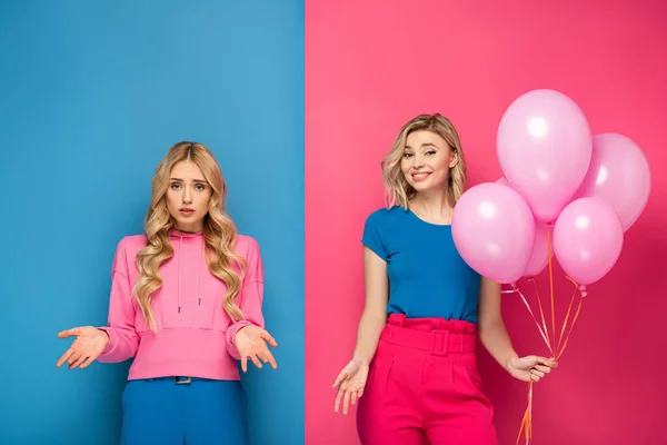 Smiling blonde girl holding balloons near offended sister on blue and pink background — Stock Photo