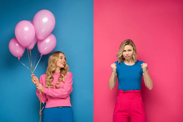 Attractive blonde girl with balloons sticking out tongue near angry sister on blue and pink background — Stock Photo