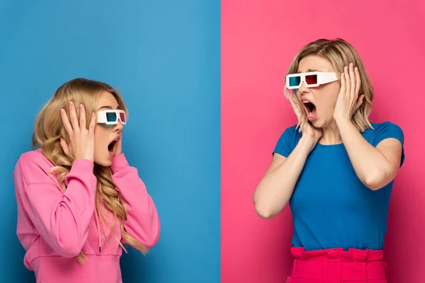 Shocked blonde girls in 3d glasses looking at each other on blue and pink background — Stock Photo