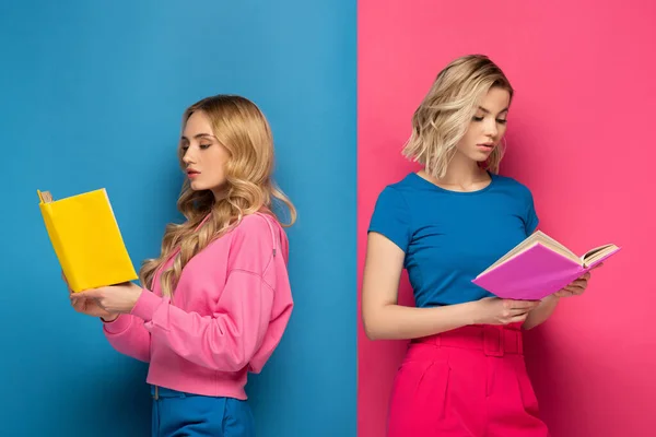 Atractivas mujeres rubias leyendo libros sobre fondo azul y rosa - foto de stock