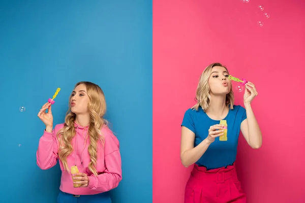 Young blonde sisters blowing soap bubbles on pink and blue background — Stock Photo