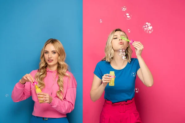 Attractive blonde women blowing soap bubbles on pink and blue background — Stock Photo