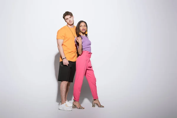 Vista completa de pareja interracial con estilo en ropa brillante posando sobre fondo blanco - foto de stock