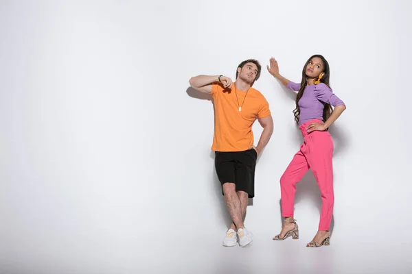 Vista completa de joven pareja interracial con estilo en ropa brillante posando sobre fondo blanco - foto de stock