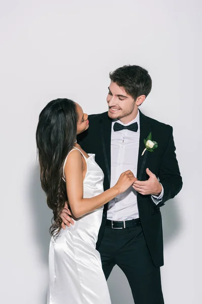 Glückliche, elegante interrassische Brautpaare, die einander auf weißem Hintergrund anschauen — Stockfoto