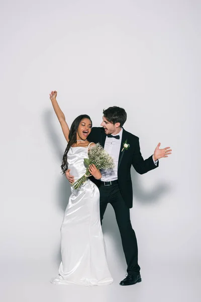 Full length view of happy, elegante interracial newlyweds dancing on white background — Fotografia de Stock