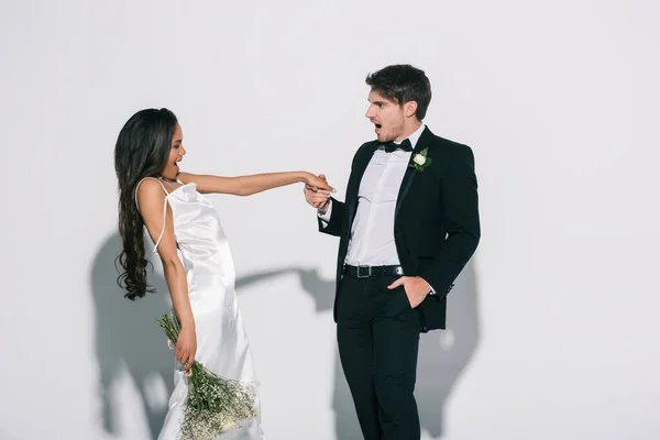 Excited bridegroom holding hand of happy african american bride on white background — Stock Photo