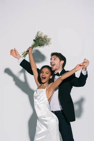 Animado, elegante interracial recém-casados dançando no fundo branco — Fotografia de Stock