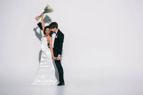 Full length view of young, elegante interracial newlyweds dancing on white background — Fotografia de Stock