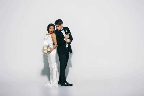Full length view of elegant interracial newlyweds standing back to back on white background — Stock Photo
