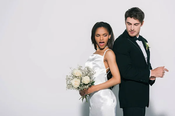 Handsome bridegroom and attractive african american bride standing back to back on white background — Stock Photo