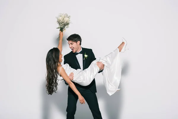 Sposo eccitato tenendo felice sposa afro-americana su mani su sfondo bianco — Foto stock