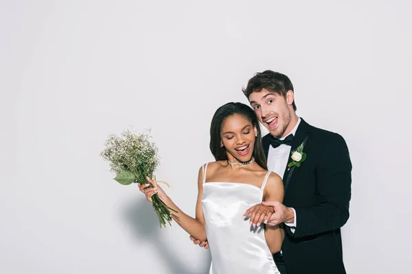 Noivo feliz mostrando casamento na mão da noiva americana africana bonita no fundo branco — Fotografia de Stock