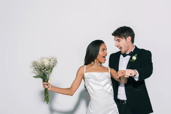 Animado interracial recém-casados mostrando anéis de casamento em suas mãos no fundo branco — Fotografia de Stock