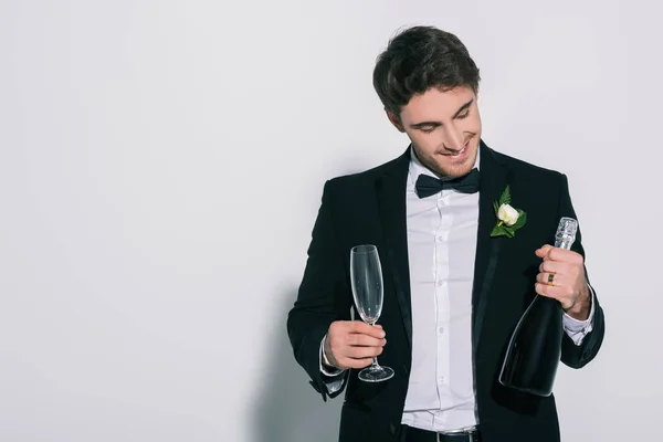 Noivo sorrindo segurando copo de champanhe e garrafa no fundo branco — Fotografia de Stock