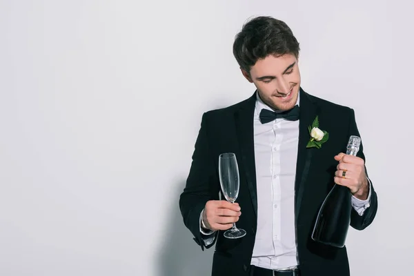 Novio sonriente sosteniendo copa de champán y botella sobre fondo blanco — Stock Photo