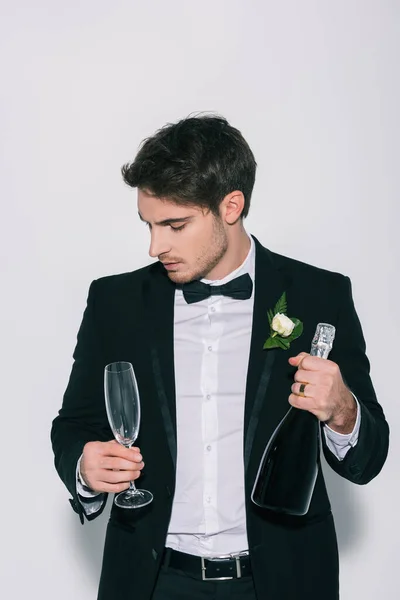 Pensive bridegroom holding champagne glass and bottle on white background — Stock Photo