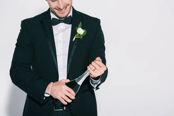 Обрізаний вид усміхненого нареченого відкриває пляшку шампанського на білому тлі — стокове фото