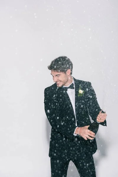 Happy bridegroom opening bottle near splashes of champagne on white background — Stock Photo