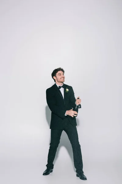 Visão de comprimento total do noivo feliz abrindo champanhe no fundo branco — Fotografia de Stock