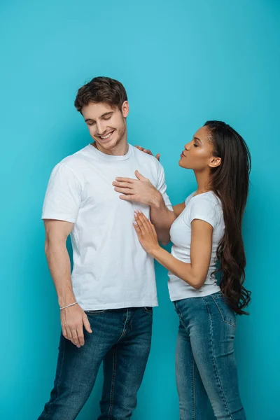 Pretty african american girl touching smiling, shy boyfriend on blue background — Stock Photo