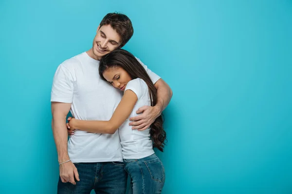 Heureux couple interracial embrasser avec les yeux fermés sur fond bleu — Photo de stock