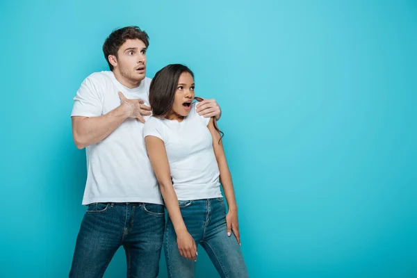 Couple interracial effrayé regardant loin sur fond bleu — Photo de stock