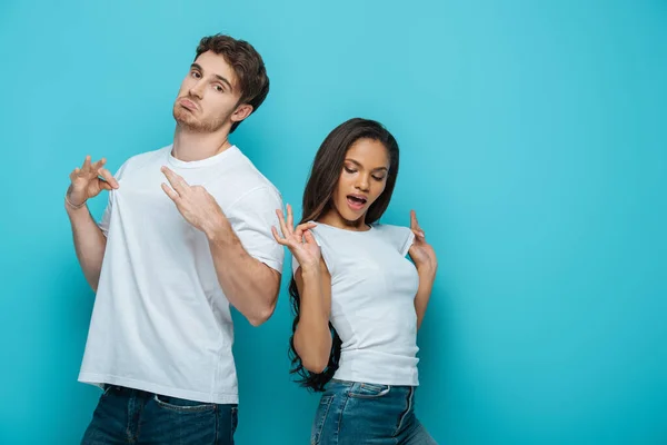 Skeptischer Mann und kokette afrikanisch-amerikanische Mädchen berühren weißes T-Shirt auf blauem Hintergrund — Stockfoto