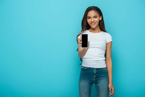 Sorridente menina americana africana mostrando smartphone com tela em branco isolado no azul — Fotografia de Stock