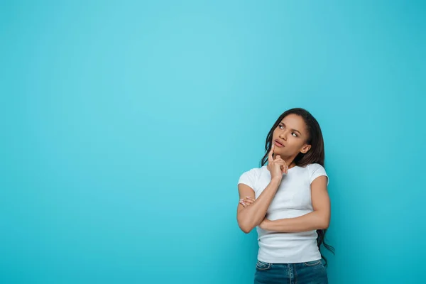 Reflexiva afroamericana chica tocando la barbilla mientras mira hacia otro lado aislado en azul - foto de stock