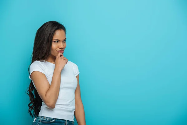 Réfléchie afro-américaine fille toucher le menton et regarder loin isolé sur bleu — Photo de stock