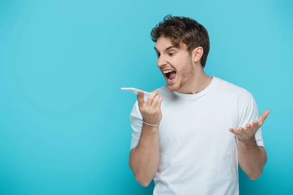 Angry young man shouting during video call on blue background — Stock Photo